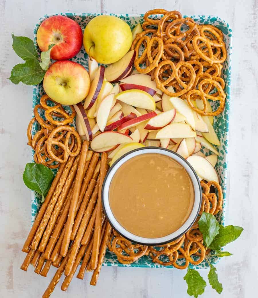 a tray with sliced apples and different shapes of pretzels surrounding a bowl of caramel dip