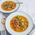 sausage and black bean pumpkin soup with a rich orange broth in two white bowls