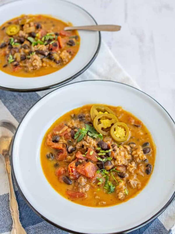 sausage and black bean pumpkin soup with a rich orange broth in two white bowls