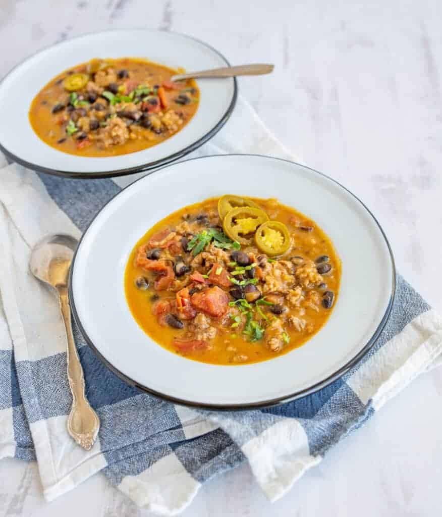 sausage and black bean pumpkin soup with a rich orange broth in two white bowls
