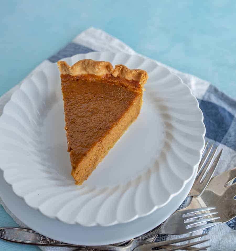 A piece of pumpkin pie on a white dessert plate. 