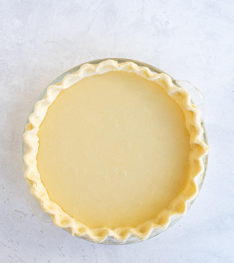 A perfect pie with pinched crust and a yellow inside is in a clear pie dish on a white marbled counter.