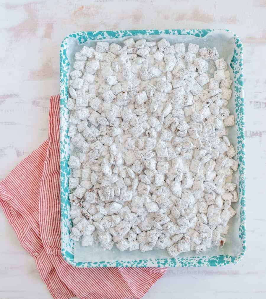chex cereal coated with powdered sugar on wax paper in a blue speckled tray sitting on red and white striped towel and white counter.