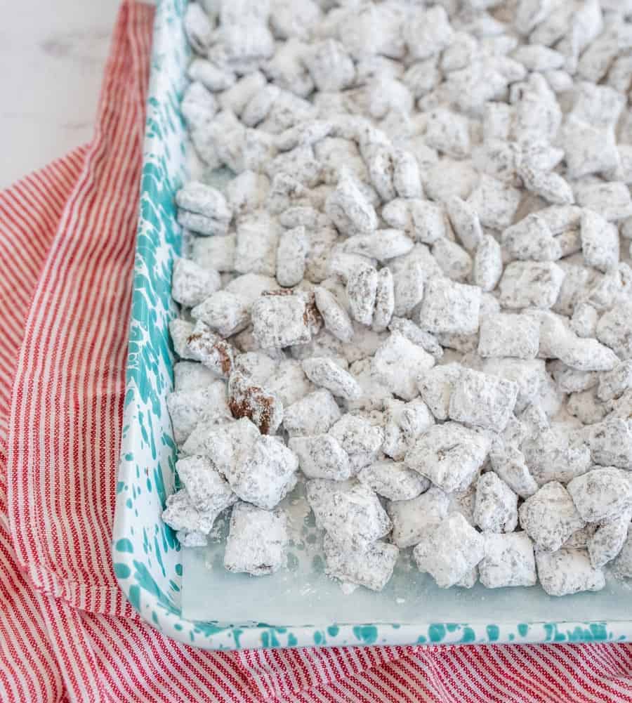 chex cereal coated with powdered sugar on wax paper in a blue speckled tray sitting on red and white striped towel and white counter.