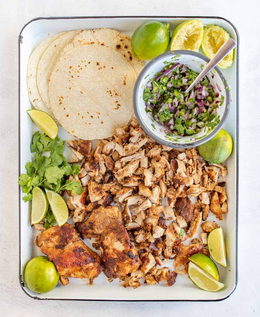 lime wedges, cilantro, red onion, chicken and tortillas on white tray