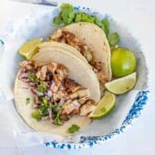 two chicken tacos on a white and blue plate