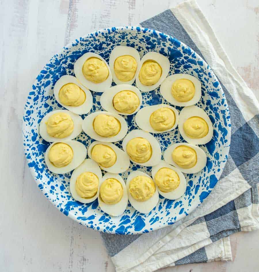 overhead image of deviled eggs in blue and white bowl on blue and white striped towel on white coutnertop