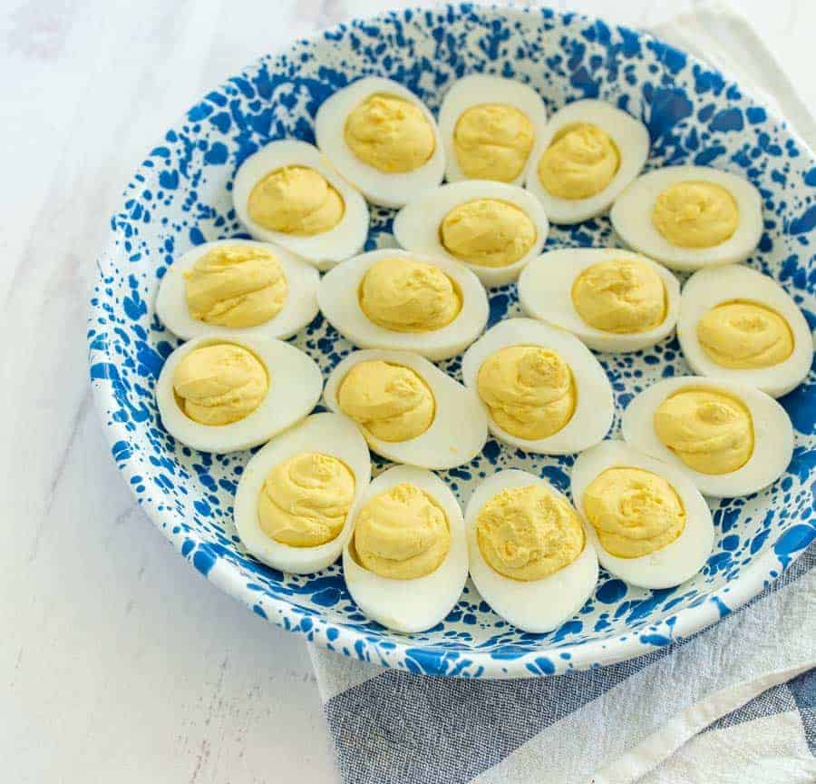 deviled eggs in blue and white specked bowl on blue and white striped towel