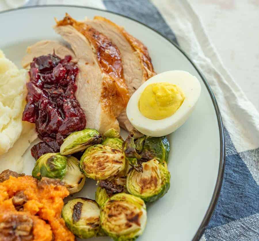 round white plate with black trim with brussels sprouts deviled eggs roast turkey sweet potato casserole cranberry sauce