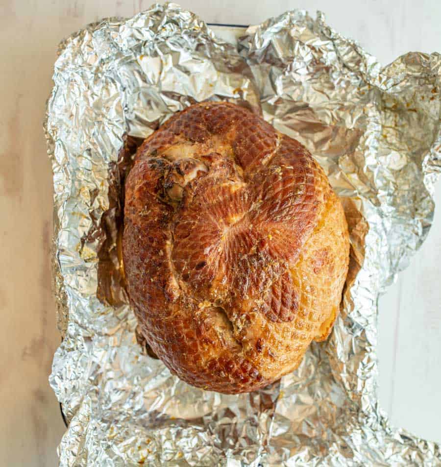 A perfectly cooked, browned ham is sitting in the middle of tin foil that covered it while cooking.