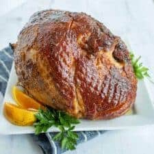 whole cooked brown sugar glazed ham on white plate