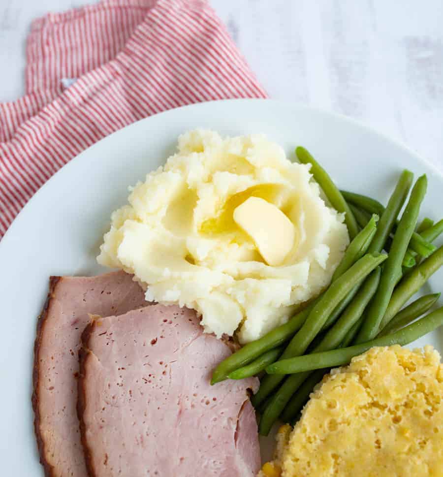 close up of mashed potatoes green beans and glazed ham on a white plate