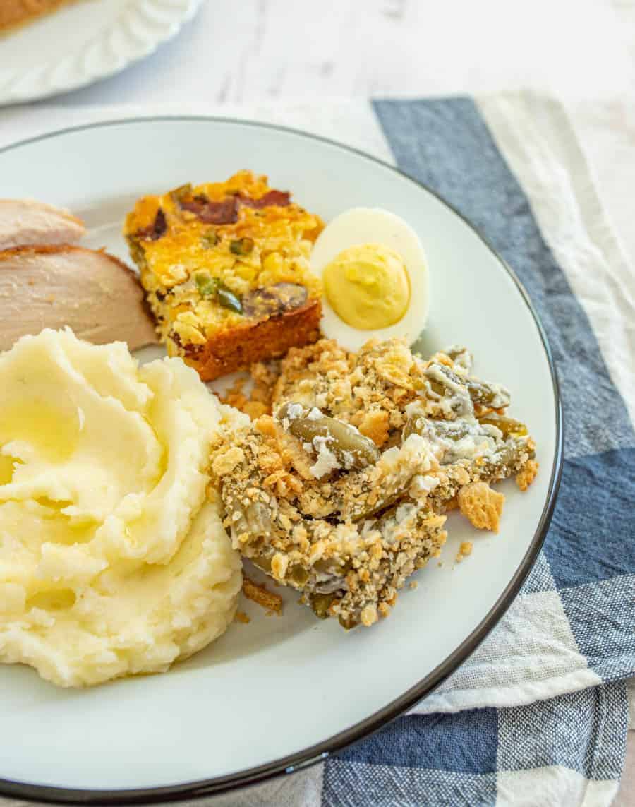 Green bean casserole with mashed potatoes turkey and deviled eggs on round white plate