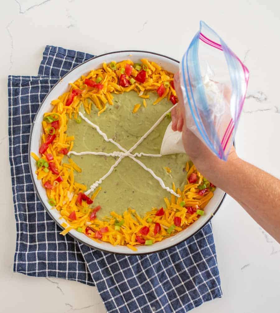 This easy Halloween bean dip is a no-bake recipe full of delicious ingredients that is SO easy to make, and its simple sour cream spider web makes it perfect to bring along to all your Halloween festivities! Wondering what to bring to this year's Halloween party? This bean dip is such a breeze to whip up (no cooking involved) and it looks intricate even though it's so easy, fast, and tasty! #beandip #layeredbeandip #refriedbeans #halloweenrecipes #halloweenbeandip #chipsanddip