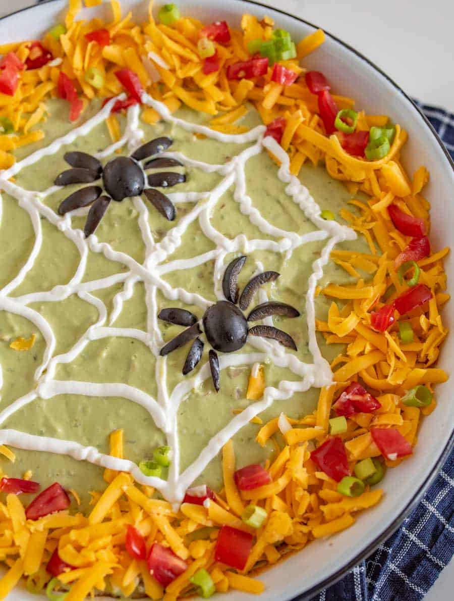 close up overhead view of a dish of Halloween bean dip with a sour cream web and black olive spiders