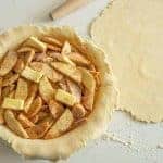 butter and seasoned apple slices inside a rolled out pie crust inside the pie dish all raw