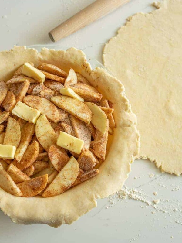 butter and seasoned apple slices inside a rolled out pie crust inside the pie dish all raw