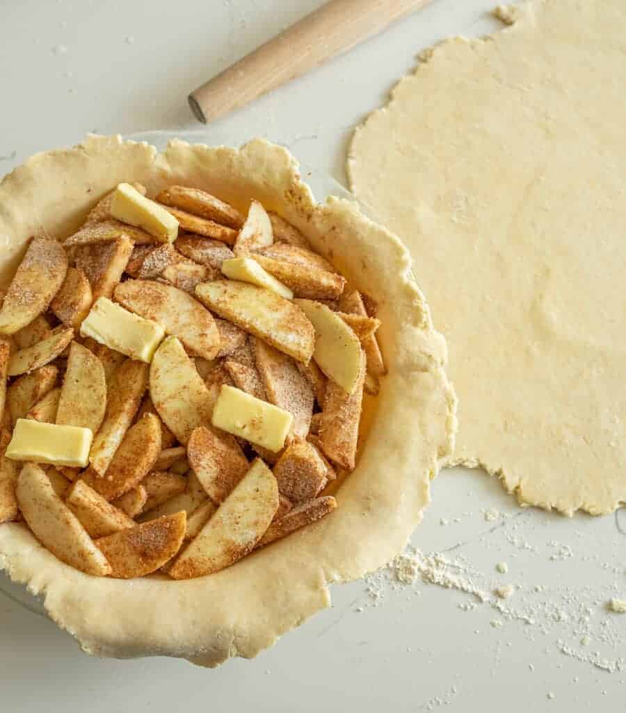 butter and seasoned apple slices inside a rolled out pie crust inside the pie dish all raw