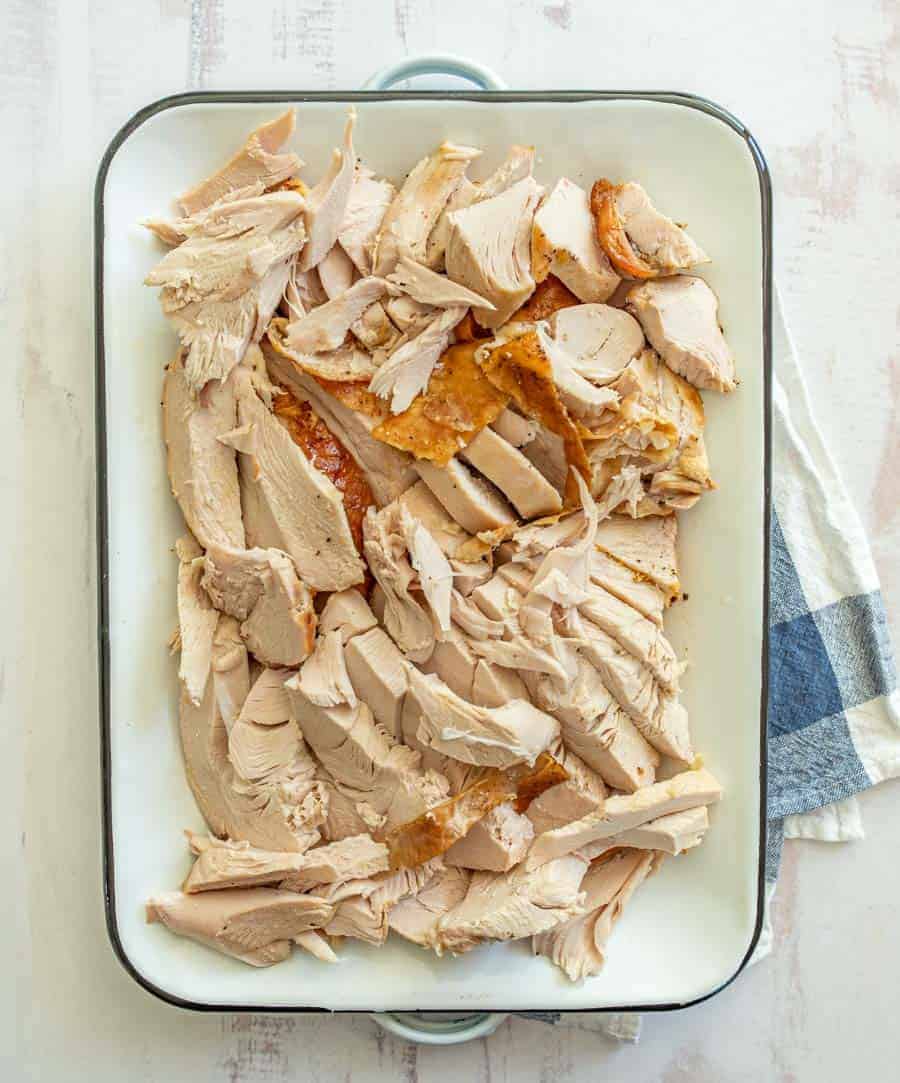 The entire turkey breast is cut up inside the white rectangle dish on top of a blue and white checkered dish towel.