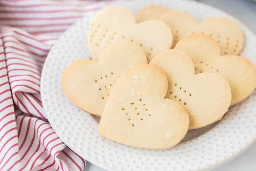 A white plate with heart shaped shortbread cookies on top of a red and white striped towel.