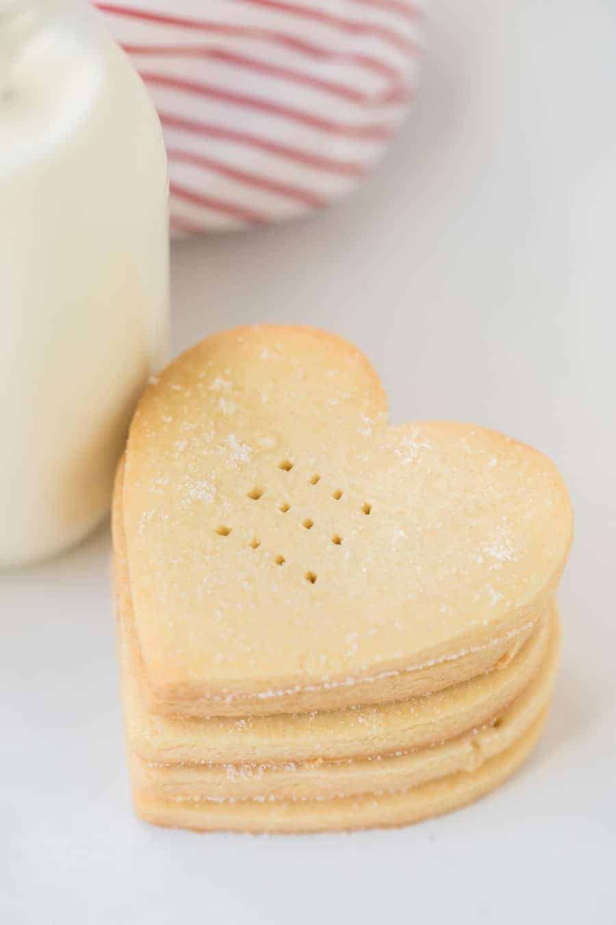 A close up of heart shaped shortbread cookies by a glass jug of milk.