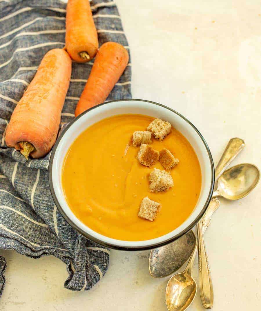 carrot soup with large homegrown carrots next to the bowl and croutons on top of the soup