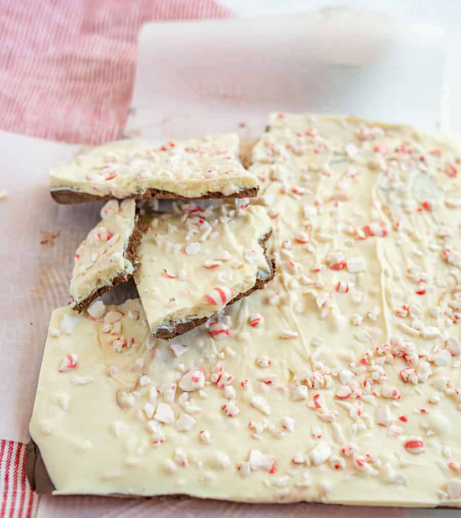 A large piece of peppermint bark on top of a red and white striped towel with a few pieces of the bark resting on the top left hand side of the bark.