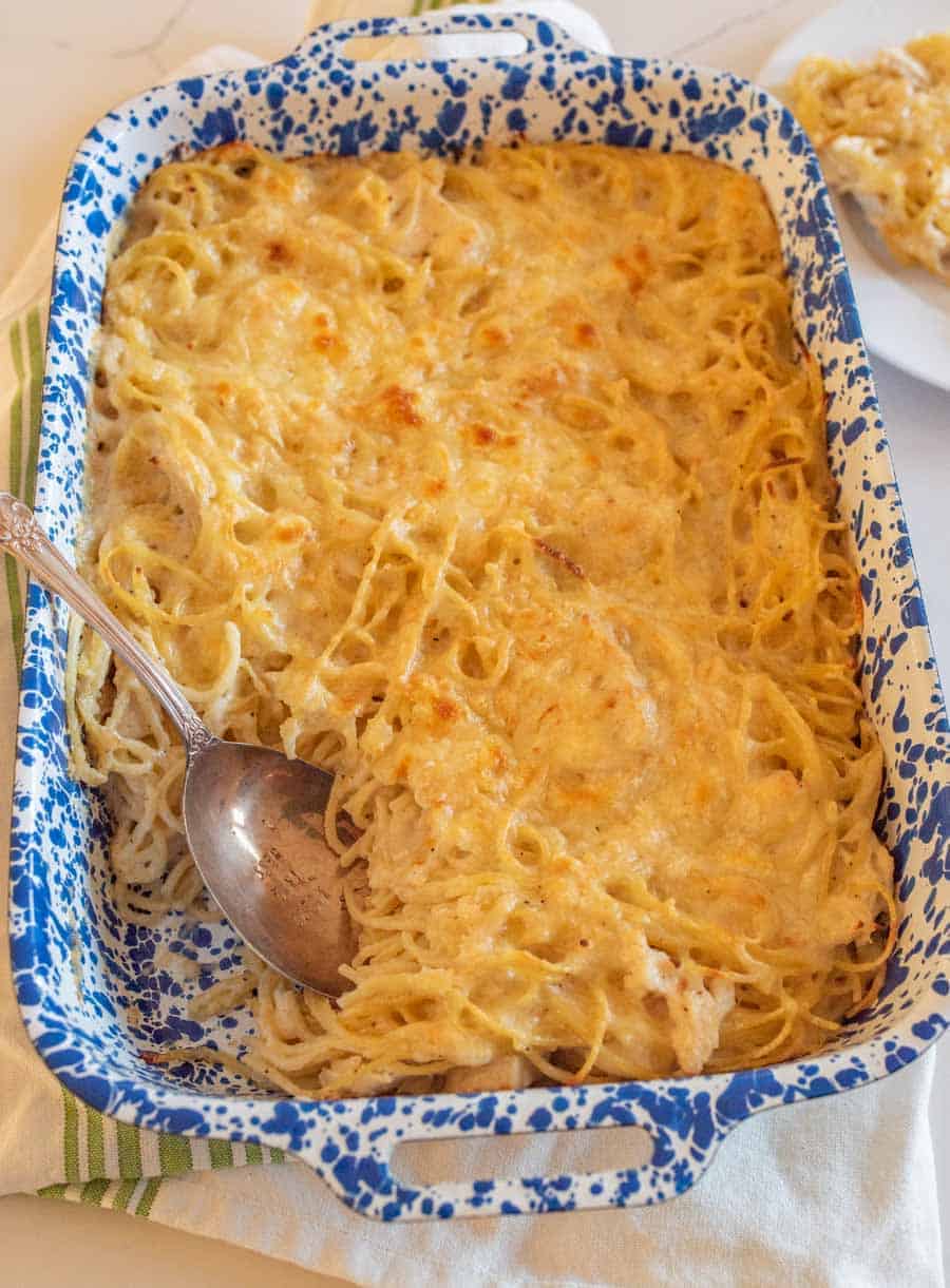 A closeup of a serving having been scooped out of the dish with a metal spoon. In the upper right-hand corner is a plate with the serving on it.