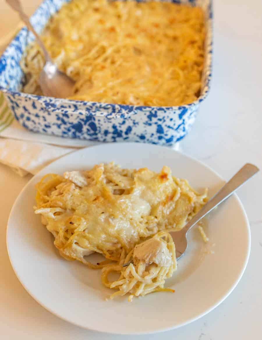 A small white plate with a serving of the turkey tetrazzini on it, including a silver fork. In the background is the dish the serving has been taken from, including a silver serving spoon.