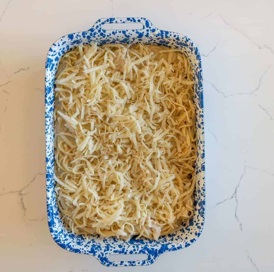 An overhead shot of the pasta all mixed, covered in grated cheese inside a ceramic rectangular pan that is white with bright blue speckles, on top of a white granite counter top.