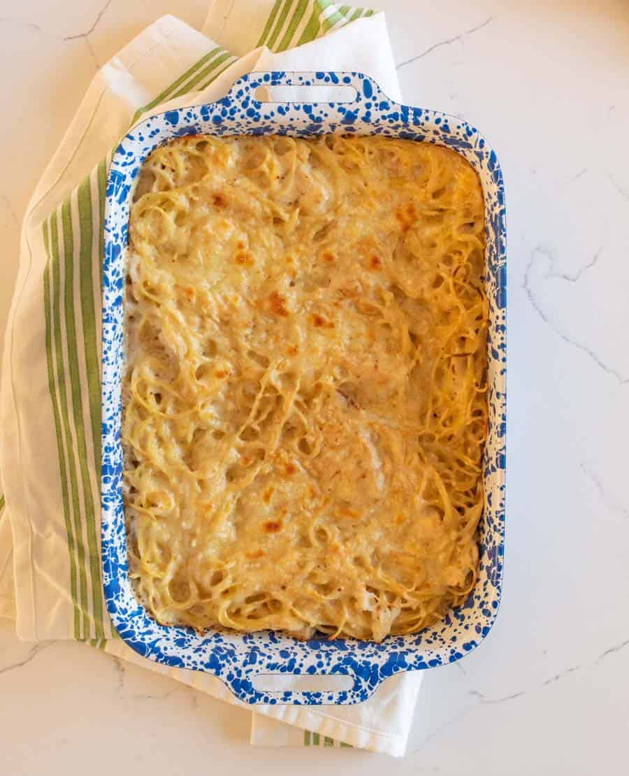 An overhead shot of the cooked dish inside a rectangular white ceramic pan that is speckled with bright blue, resting on a white dish towel with some green stripes down it.