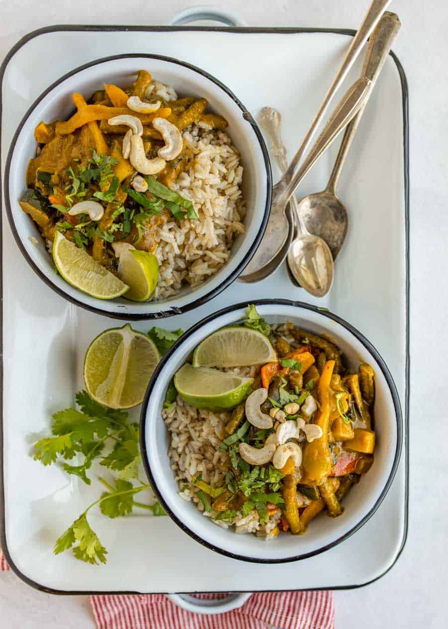 two bowls of veggie curry on white serving dish with spoons