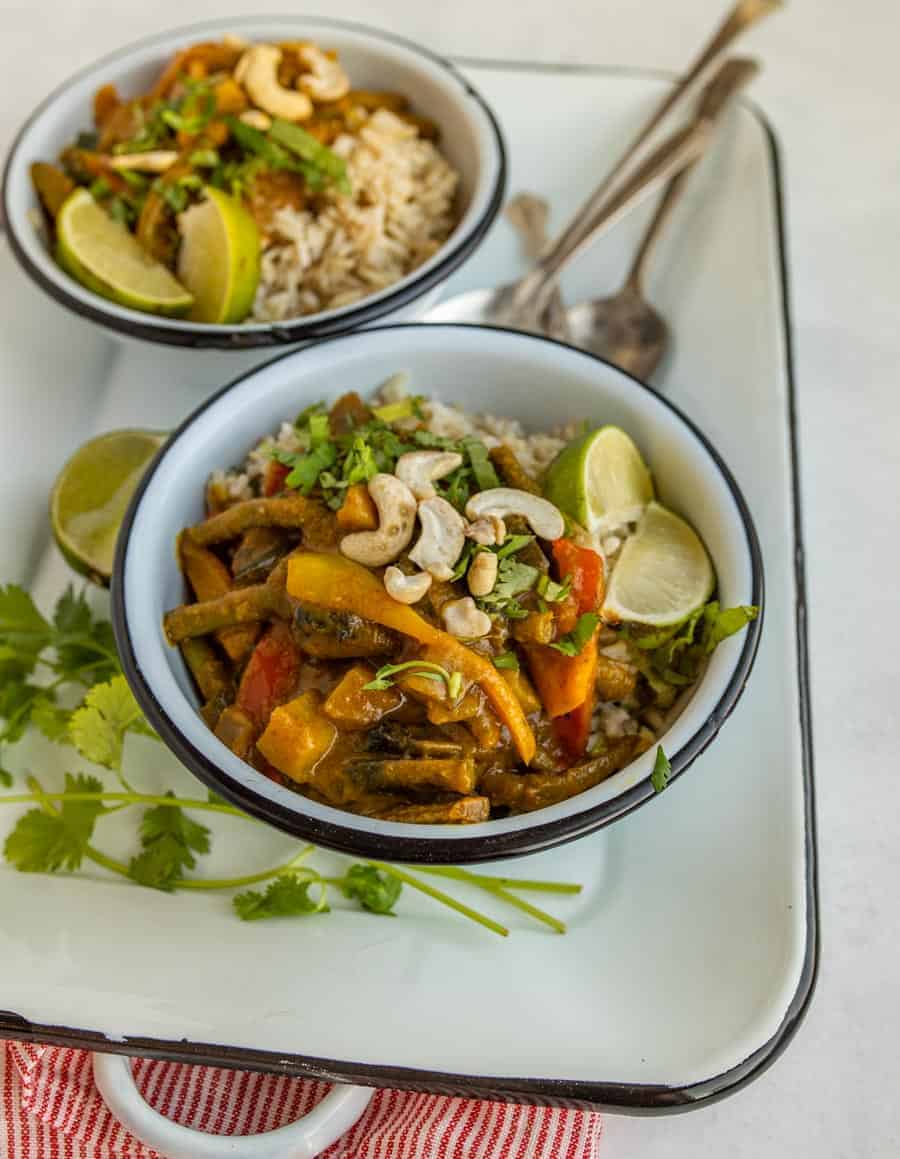 two bowls of veggie curry on white serving dish with spoons