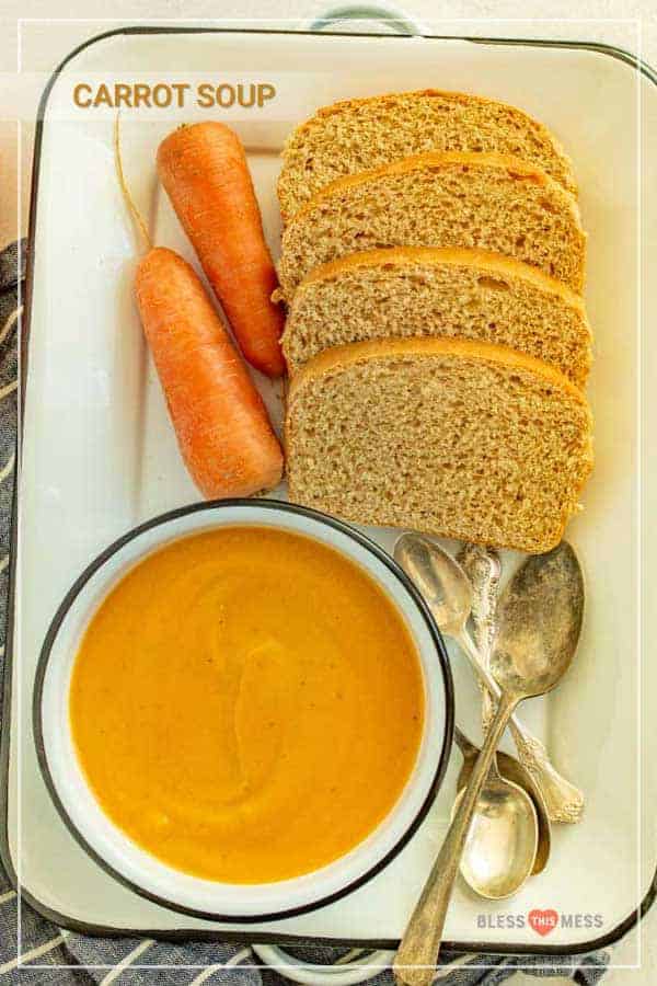 Title Image for Carrot Soup and a rectangular serving dish with a bowl of carrot soup, whole carrots, several slices of bread and a few spoons