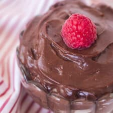 top view of chocolate pudding in a glass parfait dish with a raspberry on top