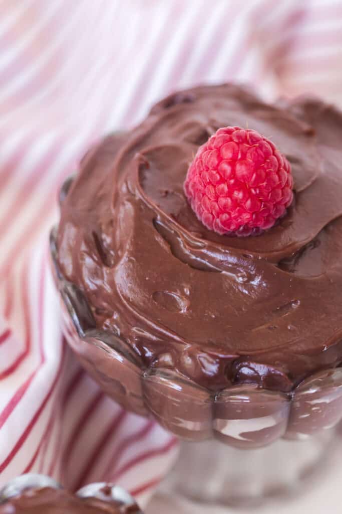 top view of chocolate pudding in a glass parfait dish with a raspberry on top