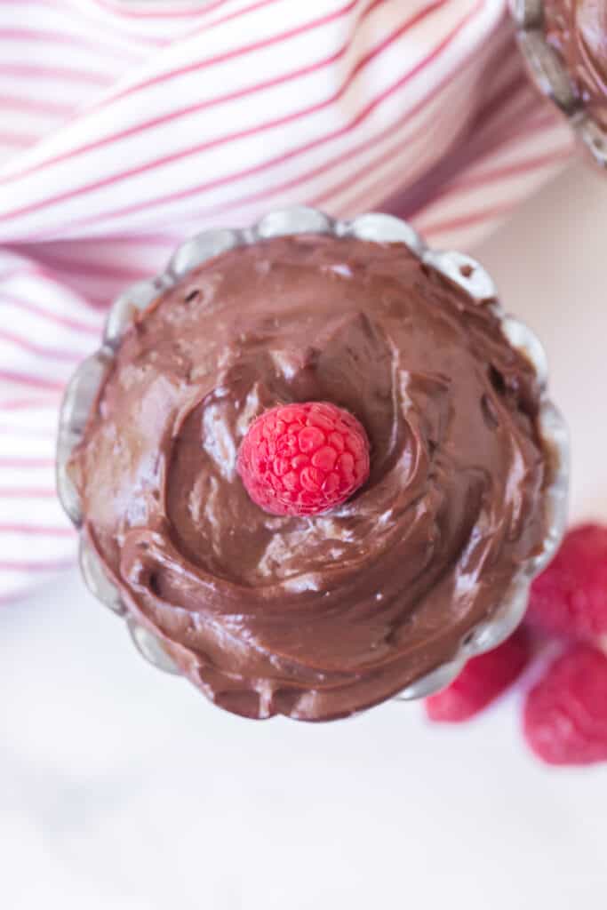 top view of chocolate pudding in a glass parfait dish with a raspberry on top