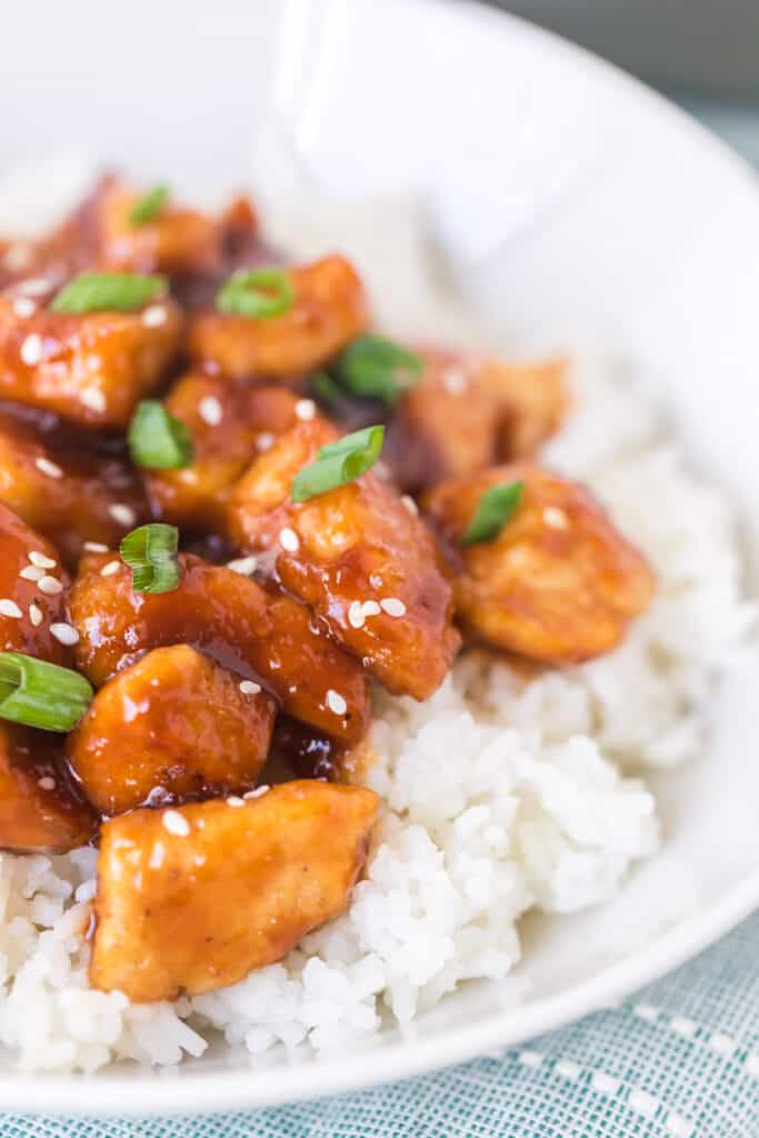 sticky general tso's chicken pieces over rice in a white bowl up close