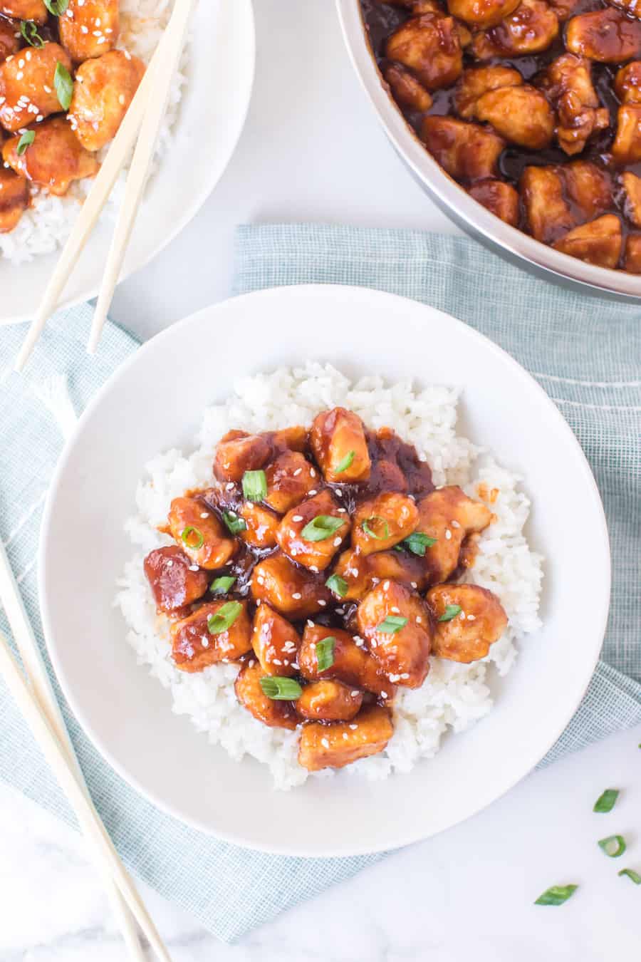 General Tso's chicken with white rice on white dish with skillet of general tso's