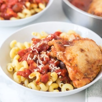 chicken with tomato sauce over garlic twisty pasta in a white bowl