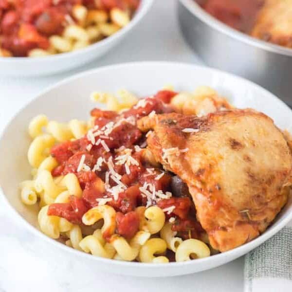 chicken with tomato sauce over garlic twisty pasta in a white bowl