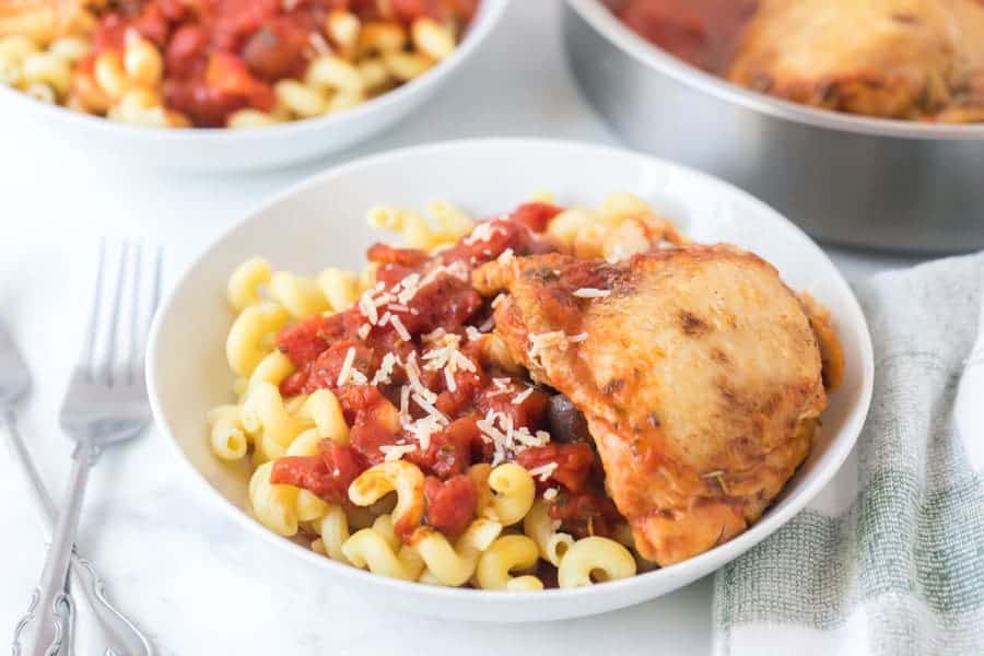 tomato and garlic pasta with chicken thigh in white bowls with forks