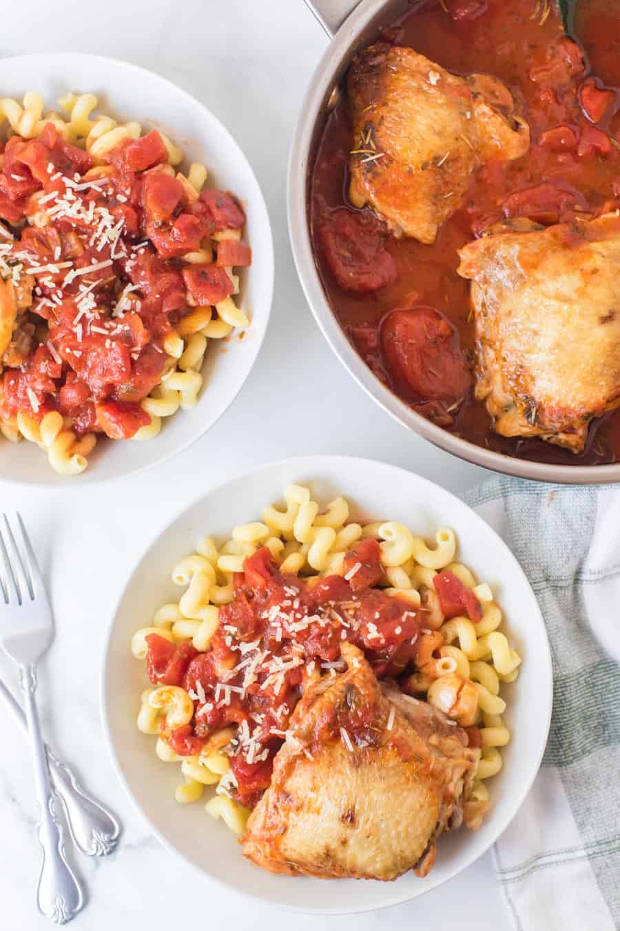 tomato and garlic cavatappi pasta with chicken thigh in white bowls and chicken thighs with garlic tomato sauce in skillet