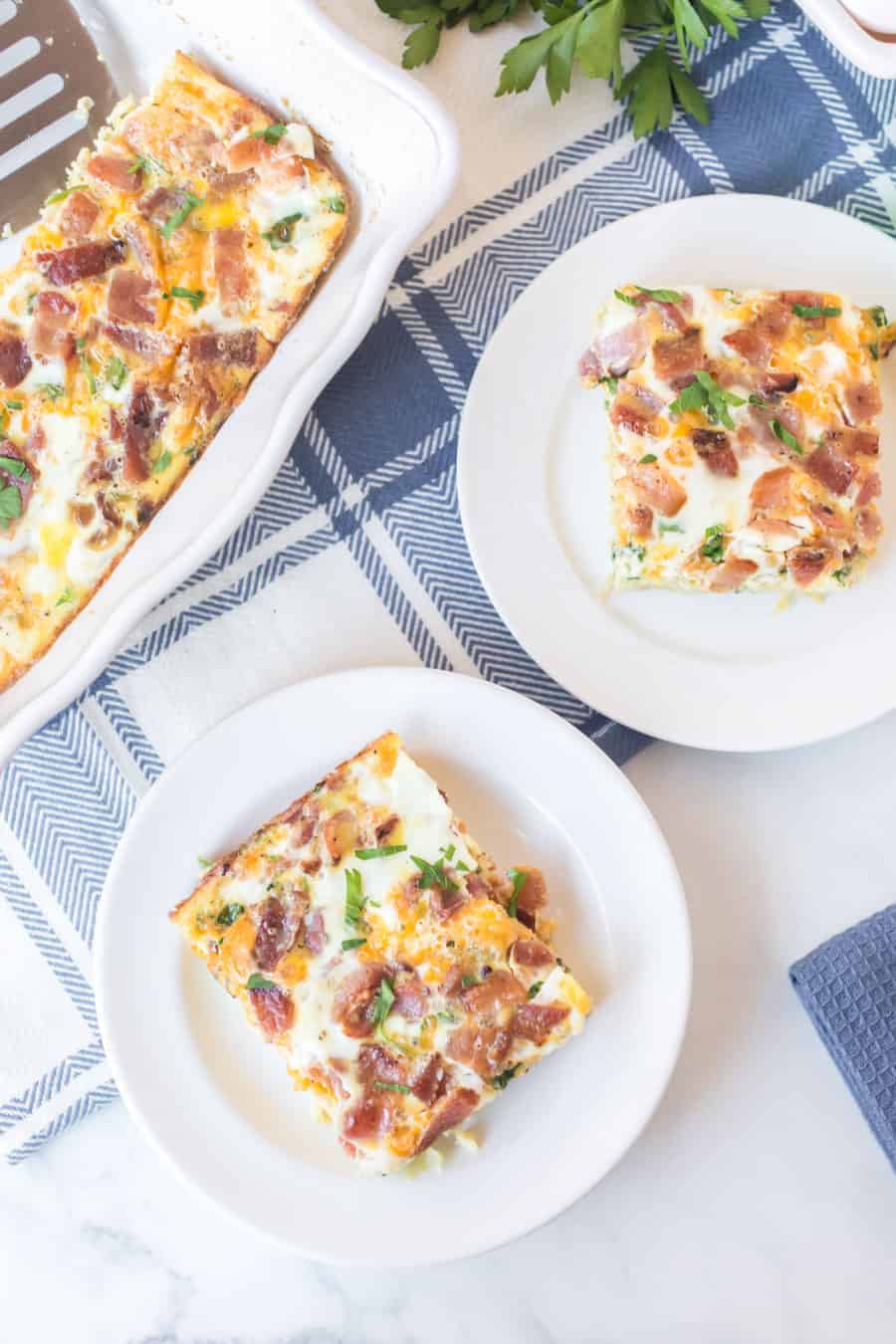 slices of bacon and cheese bake on round white plates next to casserole on blue and white checked towel