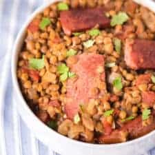 top view of a white bowl of spicy lentils and sausage with a spoon