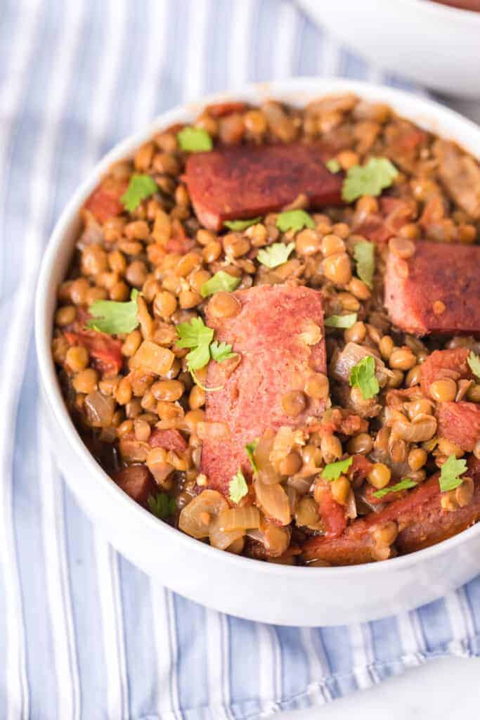 top view of a white bowl of spicy lentils and sausage with a spoon