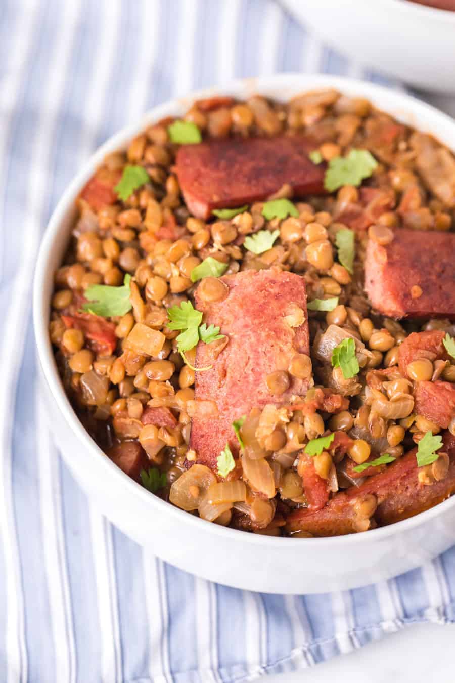 closeup image of spicy lentils and sausage in white bowl on blue and white striped towel