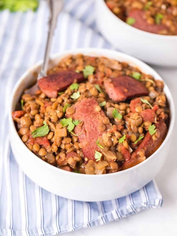 spicy lentils with sausage in white bowls with fork