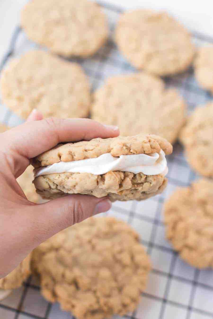 woman holding oatmeal cream pie with oatmeal cookies on cooling rack