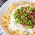 close up - pea and bacon pasta with a thick white sauce over pasta